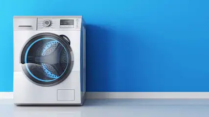 A white washing machine stands against a blue wall. The floor is light gray.