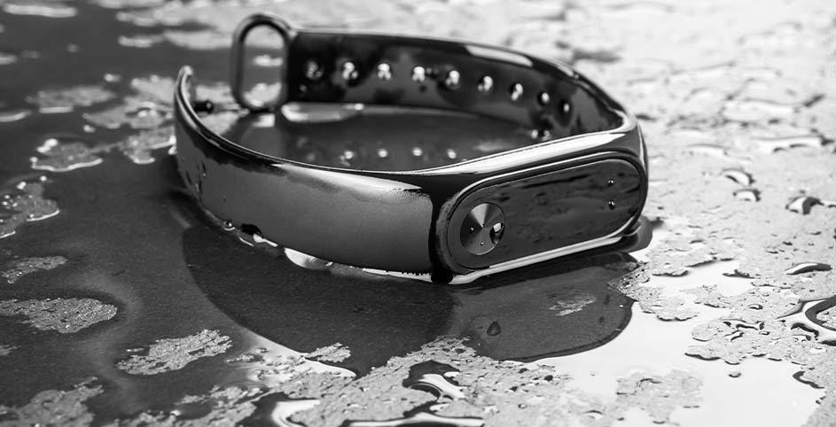 A fitness tracker with a perforated band rests on a wet surface, reflecting its form in the water droplets.