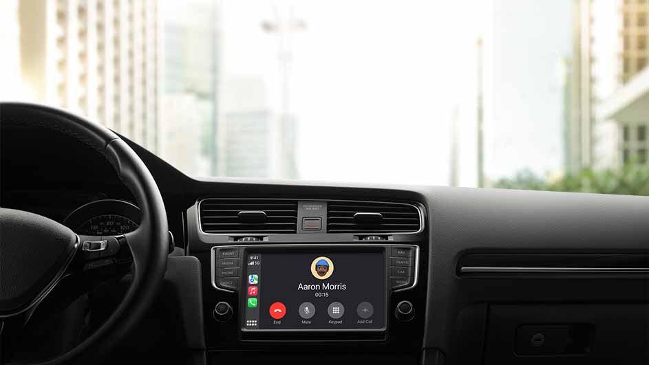 Zicht op het dashboard van een auto met een actief telefoongesprek op het scherm van het infotainmentsysteem. Buitenraam met gebouwen.