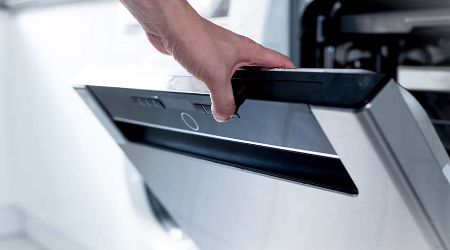 Een hand opent de deur van een zilverkleurige vaatwasser met een zwart bedieningspaneel.