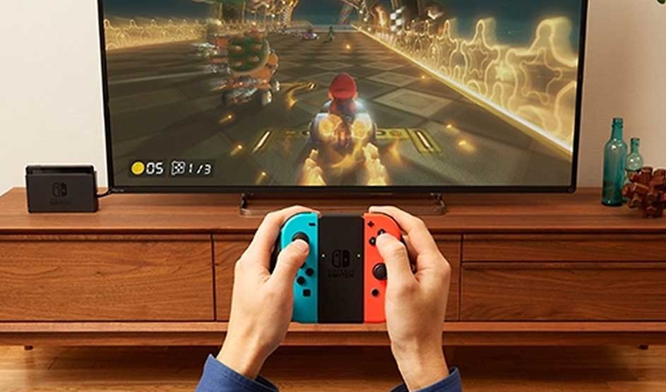 Op de afbeelding wordt Mario Kart gespeeld op een Nintendo Switch, zichtbaar aan de Joy-Con controllers en het Nintendo Switch dock bij de tv.