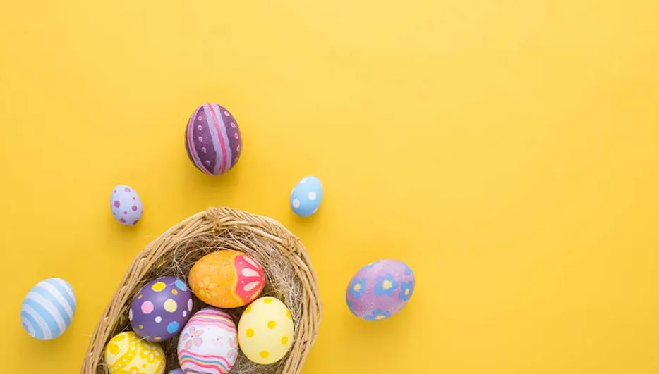 Een geelkleurige achtergrond met een gevlochten mand gevuld met versierde paaseieren in verschillende kleuren en patronen.