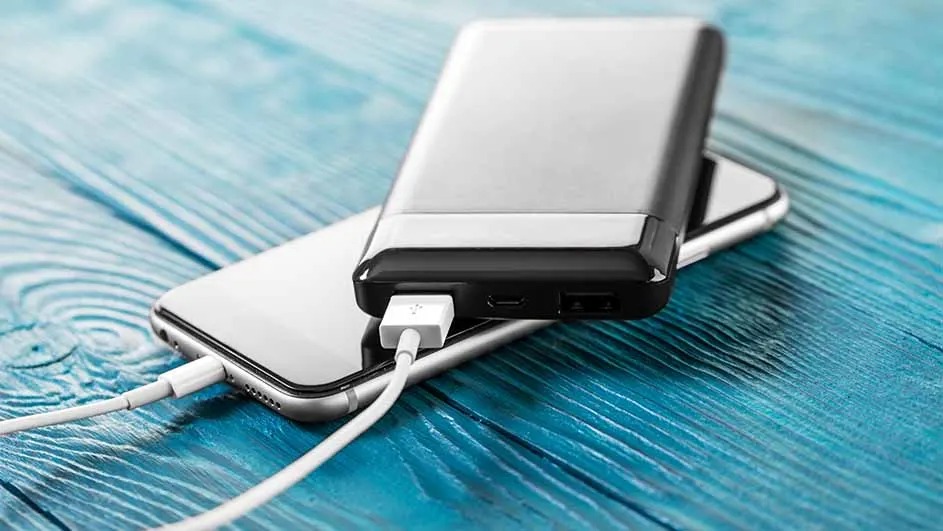 A phone and power bank sit on a blue wood surface, connected by a white cable for charging.