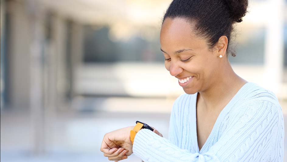 Een vrouw in een blauwe trui kijkt naar een smartwatch met een gele band. De achtergrond is wazig.
