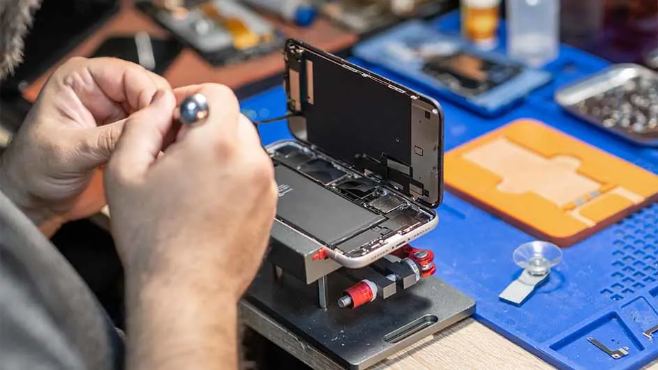 Iemand repareert een telefoon met gereedschap op een blauwe werkmat.