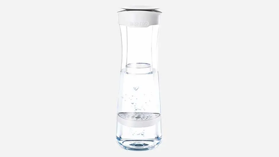 Een heldere glazen karaf met een witte boven- en onderkant, gedeeltelijk gevuld met helder water op een witte achtergrond.