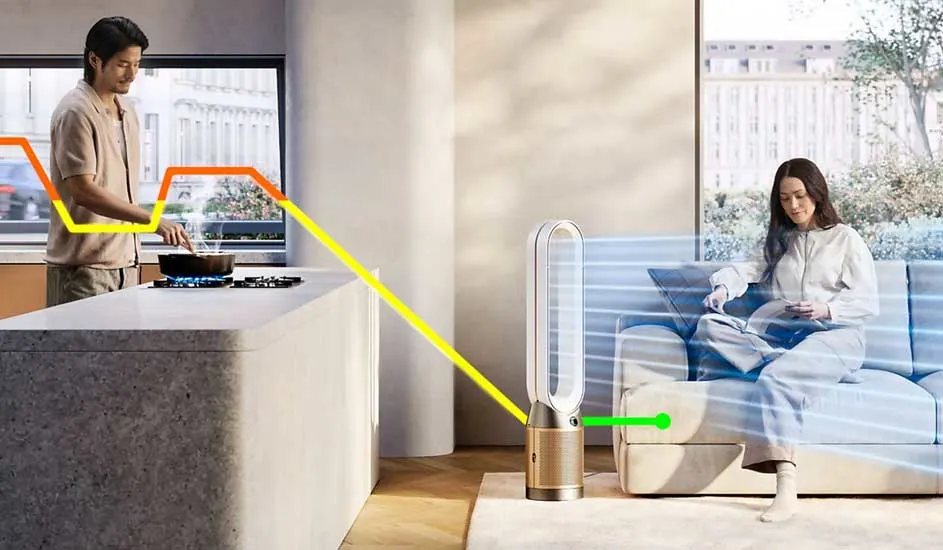 In een moderne woonkamer zit een vrouw op de bank met een boek, terwijl een Dyson luchtreiniger frisse lucht blaast richting haar. Merknaam: Dyson.