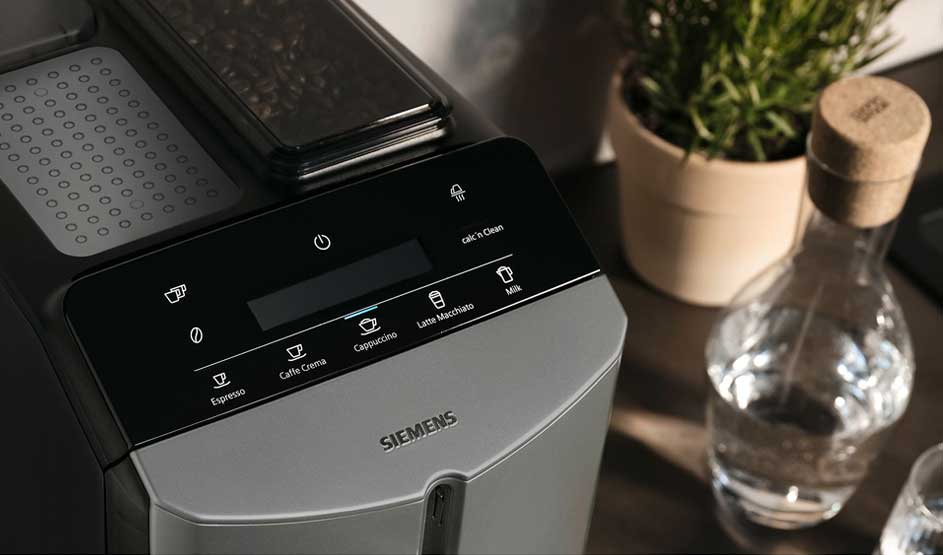 Bovenaanzicht van een Siemens koffiemachine met touchscreen, bonenreservoir, plantje en een glazen karaf water op het aanrecht.