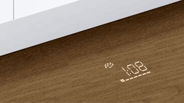 Een close-up van een houten oppervlak met een digitale projectie van "1:08" en een pictogram, onder een wit oppervlak.