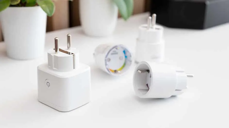 Vier witte stekkers en twee plantenpotten op een witte tafel, met een zwarte doos op de achtergrond.