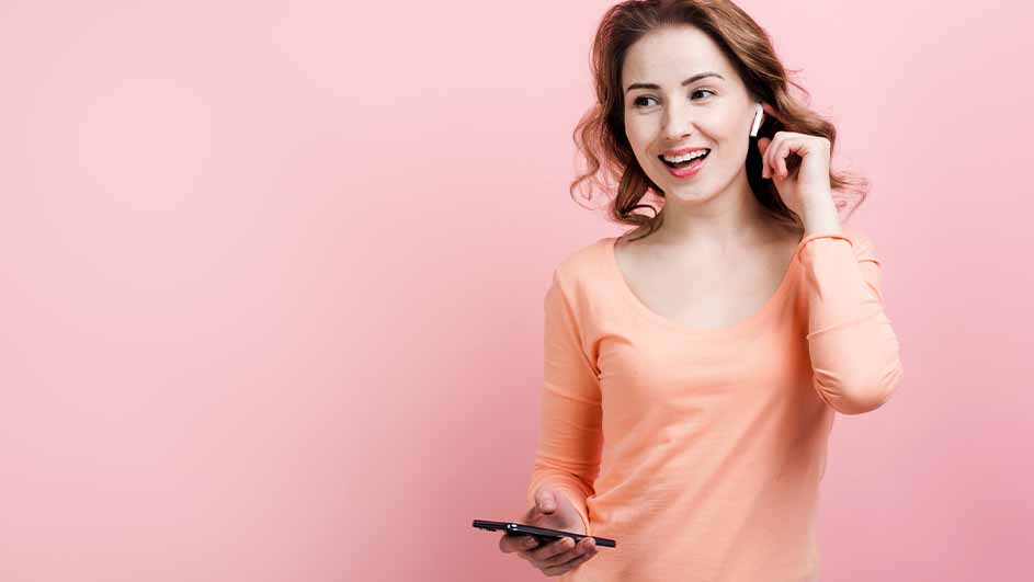 Vrouw met oortje en telefoon tegen een roze achtergrond.