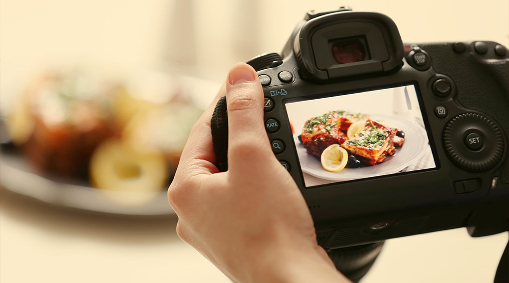 Een hand houdt een zwarte camera vast, het scherm toont een foto van een bord met gegarneerd eten en citroen.