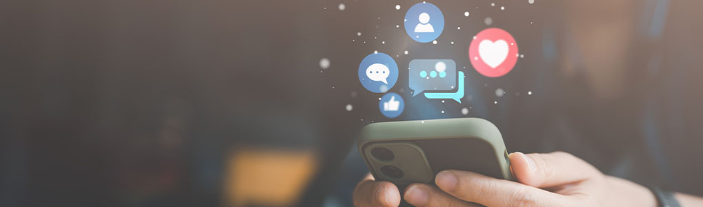 Handen houden een telefoon vast met digitale pictogrammen zoals een hart, chatballonnen en een persoon erboven.