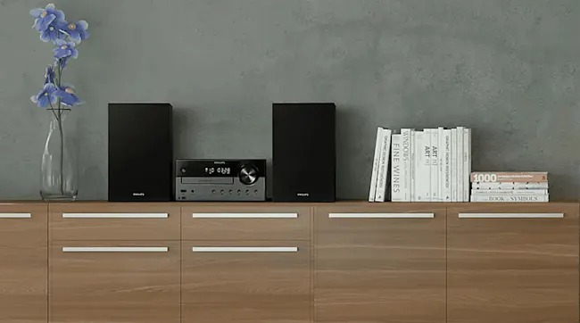 Op een houten kast staat een Philips stereoset met twee zwarte speakers en een centrale unit, naast boeken en een vaas met paarse bloemen.