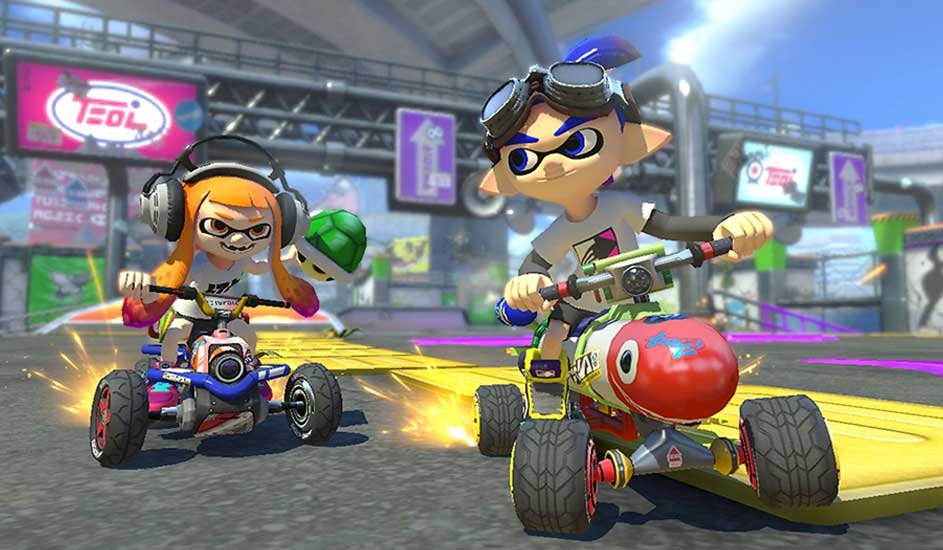Twee Splatoon-personages racen op karts in Mario Kart 8 Deluxe op een Nintendo-circuit, klaar om een groene schild te gooien.
