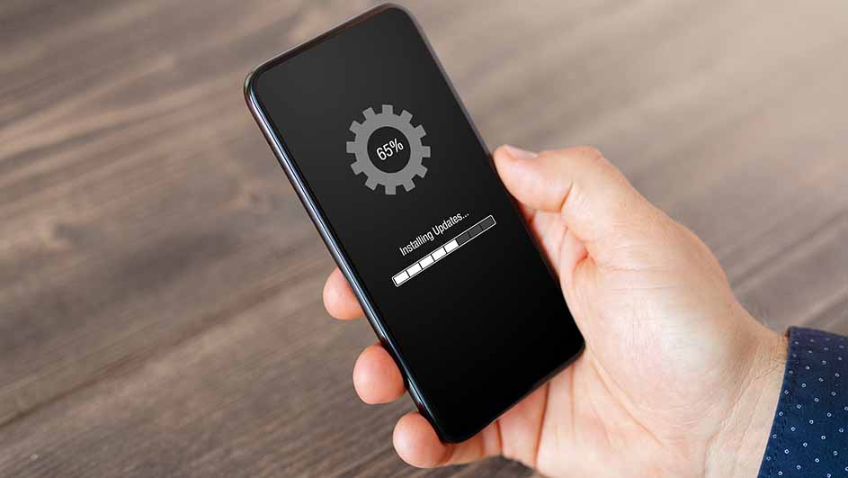 Een hand houdt een zwarte telefoon vast. Op het scherm staat 'Installing Updates...' met een voortgangsbalk op 65%.