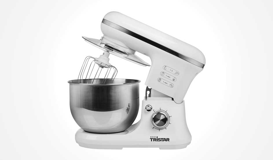 Een witte Tristar keukenmachine met metalen mengkom staat op witte achtergrond; de kop staat omhoog met garde en een grote snelheidsknop vooraan.