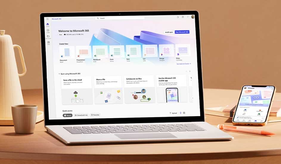 Open laptop showing Microsoft 365 home screen, with smartphone, mug and pen on a round table in warm soft lighting.