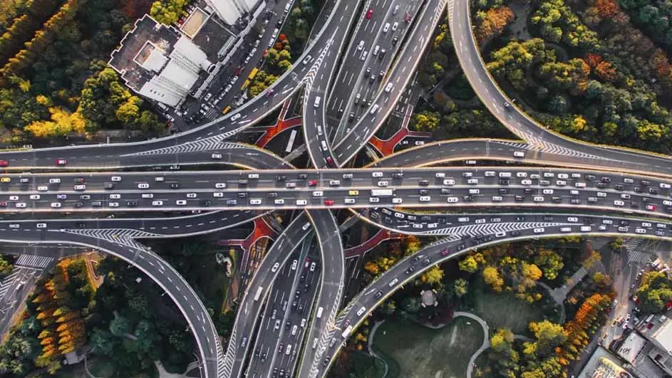Luchtfoto van een druk verkeersknooppunt met viaducten, omringd door groen en gebouwen.