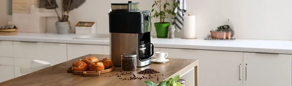A kitchen scene features a coffee maker, cup, and pastries on a table. A jar of coffee beans adds detail. The background includes white cabinets and plants.