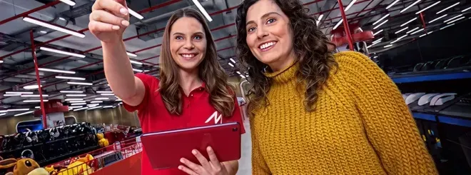 Store employee points something out to a smiling customer while holding a tablet.
