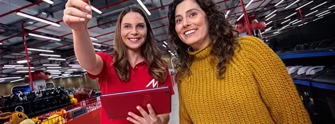 Store employee points something out to a smiling customer while holding a tablet.