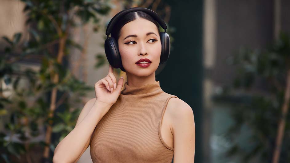 Vrouw met een bruine top en zwarte hoofdtelefoon, vinger omhoog, groene planten op de achtergrond.