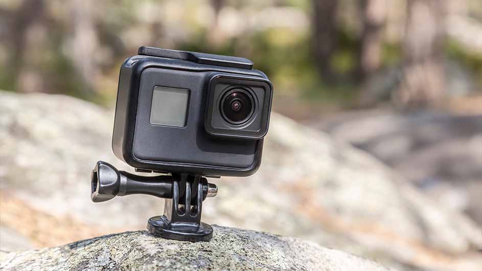 Een zwarte actiecamera staat op een grijze rots, met een vage rotsachtige achtergrond.