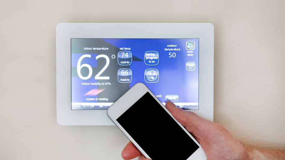 Digitale thermostaat toont 62 graden binnentemperatuur, 74 ingestelde temperatuur en 50 graden buitentemperatuur, met telefoon in hand.