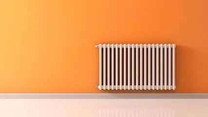 Een witte radiator hangt aan een oranje muur boven een witte plint in een kamer.
