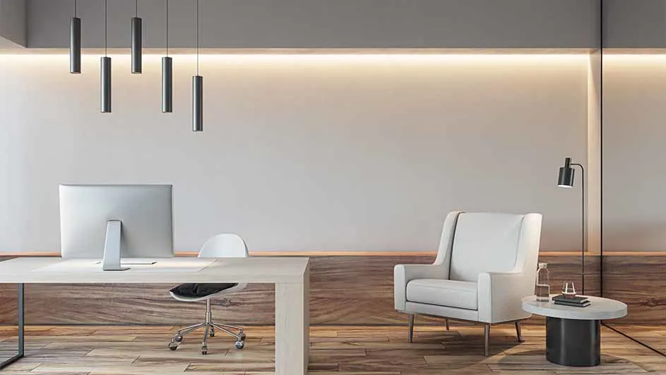 Kantoor met bureau, stoel, computer en lampen. Een witte fauteuil en bijzettafel staan aan de rechterkant. Houten vloer.