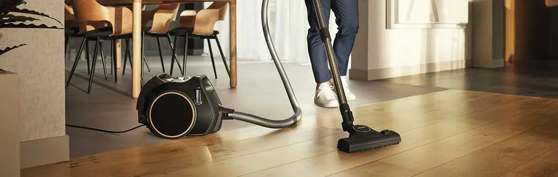 Een persoon stofzuigt een houten vloer met een klassieke sledestofzuiger, ideaal voor dagelijks schoonmaken.