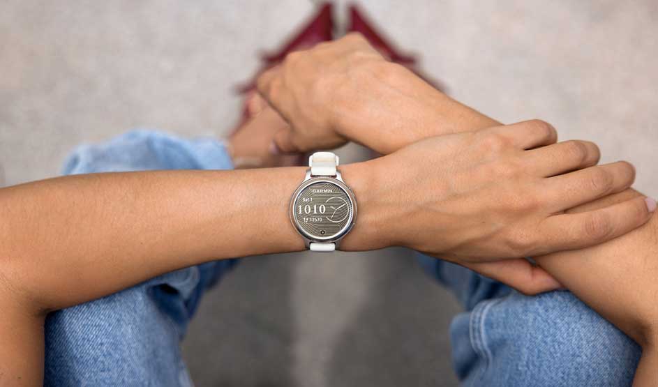 Person wearing Garmin smartwatch with white band showing time 10:10, hands clasped together, wearing blue jeans.