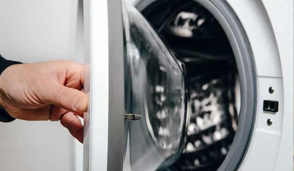 A hand is opening the door of a front-loading washing machine. The drum and door mechanism are visible, but there is no brand name shown on the appliance.