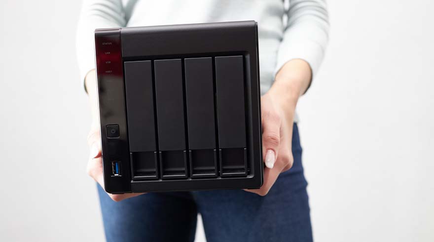 Een persoon houdt een zwarte netwerkopslagapparaat vast met ruimte voor vier harde schijven tegen een witte achtergrond.