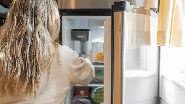 Woman reaching into an open refrigerator in a bright kitchen.
