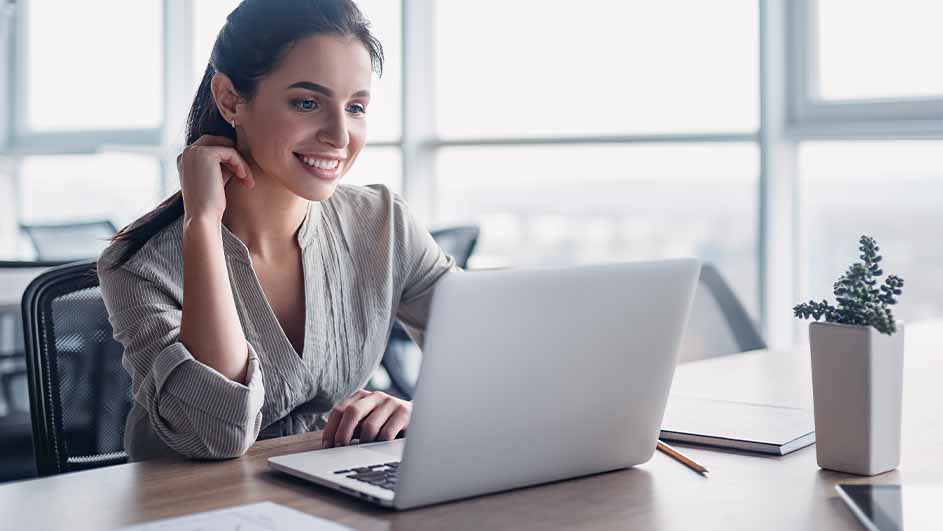 Een vrouw zit aan een bureau met een laptop, een notitieboek, een potlood en een plant in een witte pot.