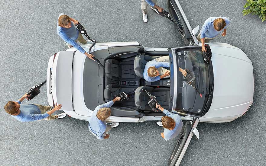 Several people work together using car vacuum cleaners to thoroughly clean every corner of a convertible car from above.