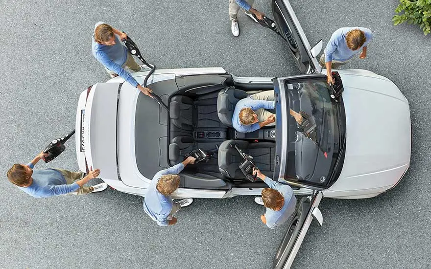 Several people work together using car vacuum cleaners to thoroughly clean every corner of a convertible car from above.