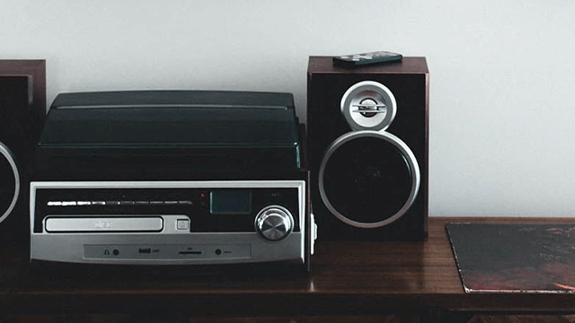 Zwarte platenspeler en zilverkleurige cd-speler naast een donkere luidspreker op een houten oppervlak.