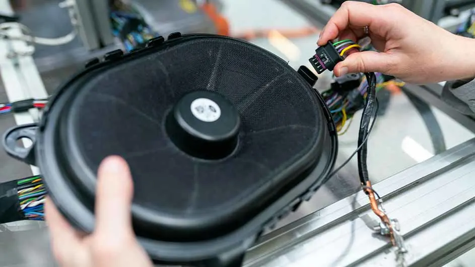 Zwarte luidspreker met een hand die een connector met draden vasthoudt, alles gemonteerd op een metalen frame.