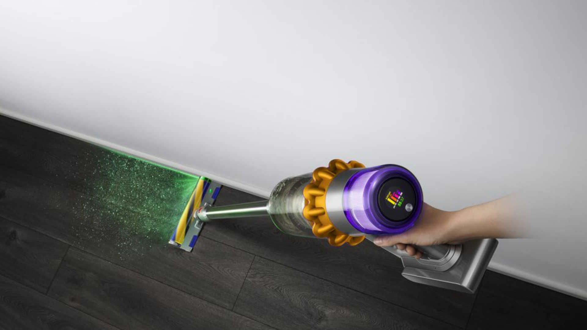 Een persoon stofzuigt een houten vloer met een paarse Dyson stofzuiger, met een groene laser op de vloer.