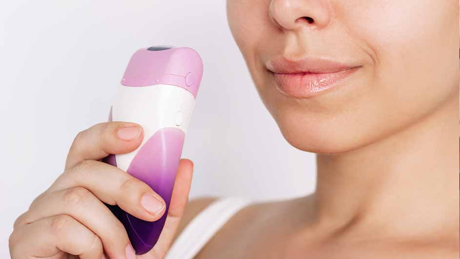 Een vrouw houdt een wit apparaat met roze en paarse accenten vast, tegen een witte achtergrond.