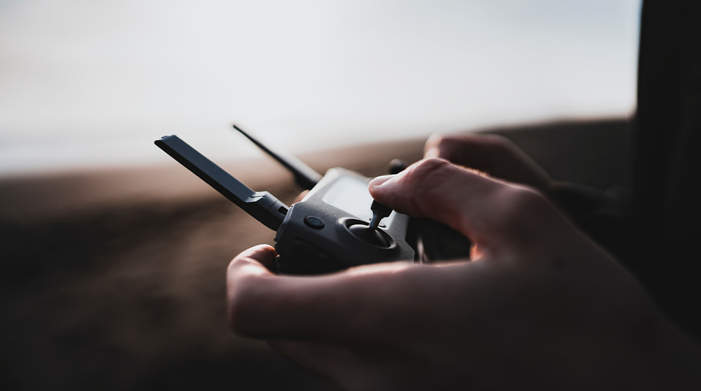 Een hand bedient een zwarte drone-afstandsbediening met twee antennes tegen een vage achtergrond.