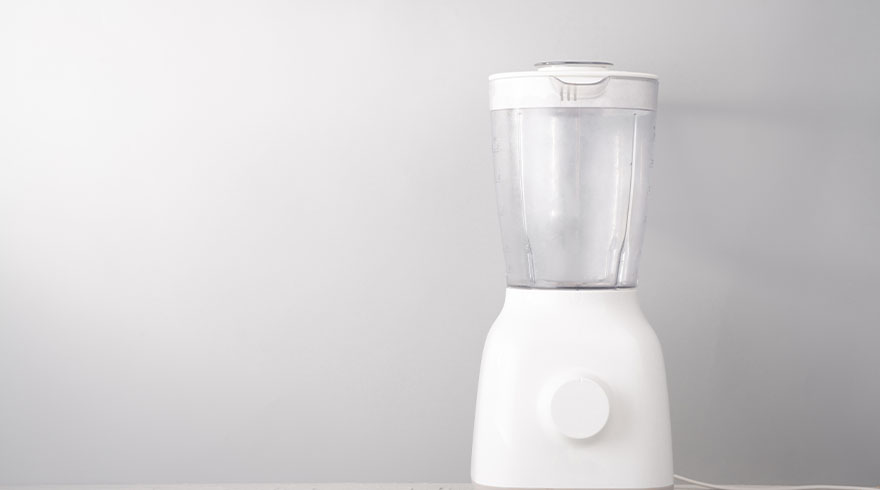 Een witte blender met een doorzichtige kan staat op een witte ondergrond tegen een witte achtergrond.