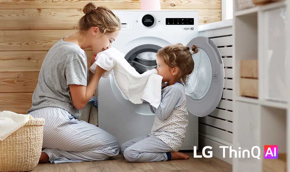 Een moeder en dochter knielen bij een open wasmachine, ruiken aan een witte handdoek en lijken samen vrolijk de was te doen.