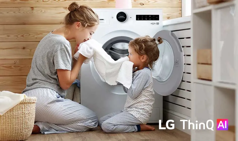 Een moeder en dochter knielen bij een open wasmachine, ruiken aan een witte handdoek en lijken samen vrolijk de was te doen.