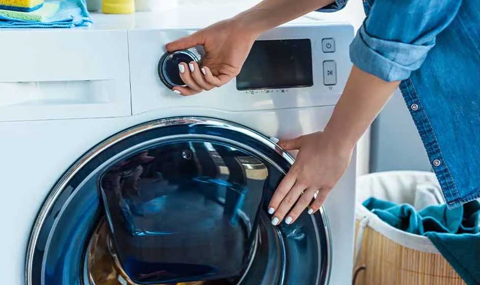 Iemand stelt een wasmachine in en houdt de deur open; de scène toont een alledaags moment in een nette wasruimte.
