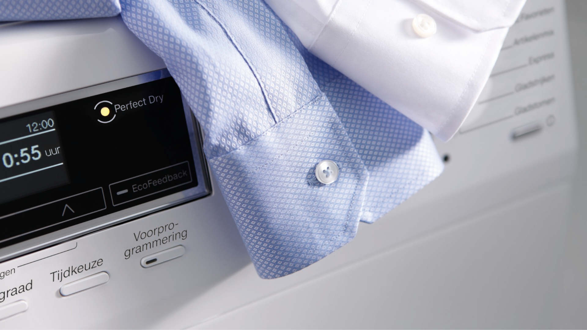 Blauw en wit overhemd op een witte wasmachine met scherm waarop 12:00 en 0:55 uur staat.