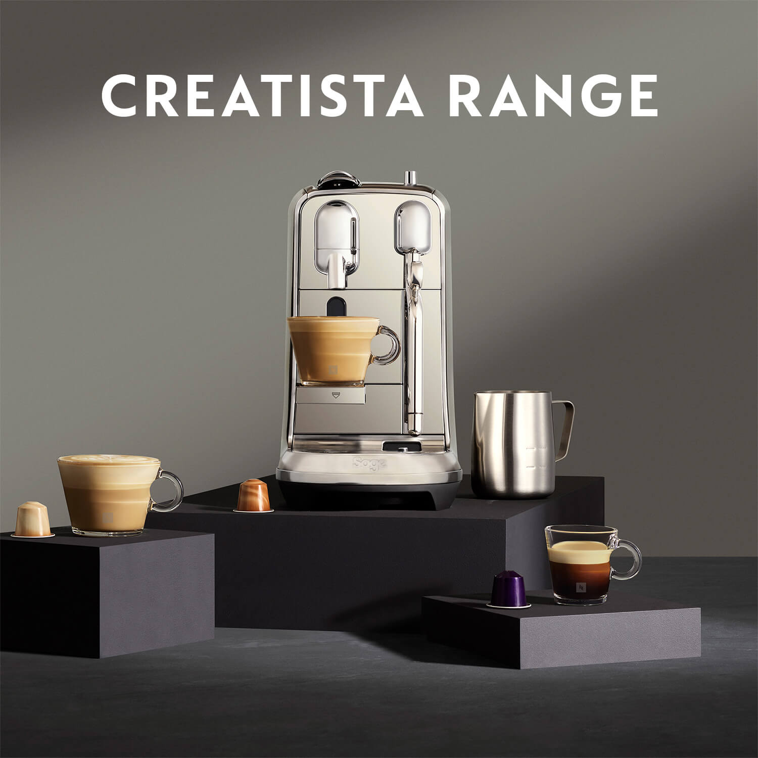 Een zilverkleurige koffiemachine met kopjes koffie en capsules op zwarte blokken tegen een grijze achtergrond.